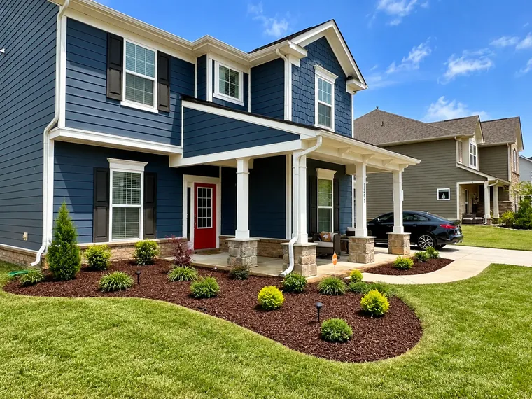 A curved mulch bed with mixed shrubs and lighting in front of a navy house
