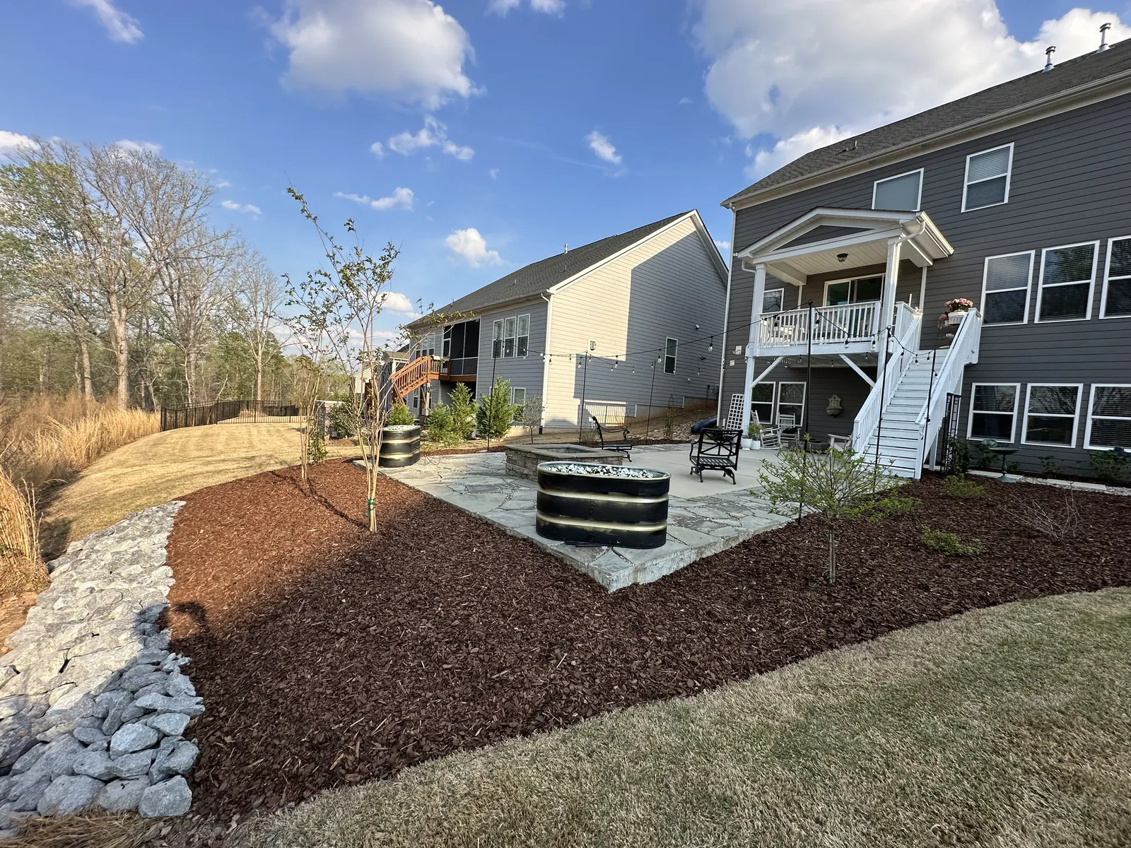 Backyard with mulched beds, a stone patio, small trees and a rock drainage runnel
