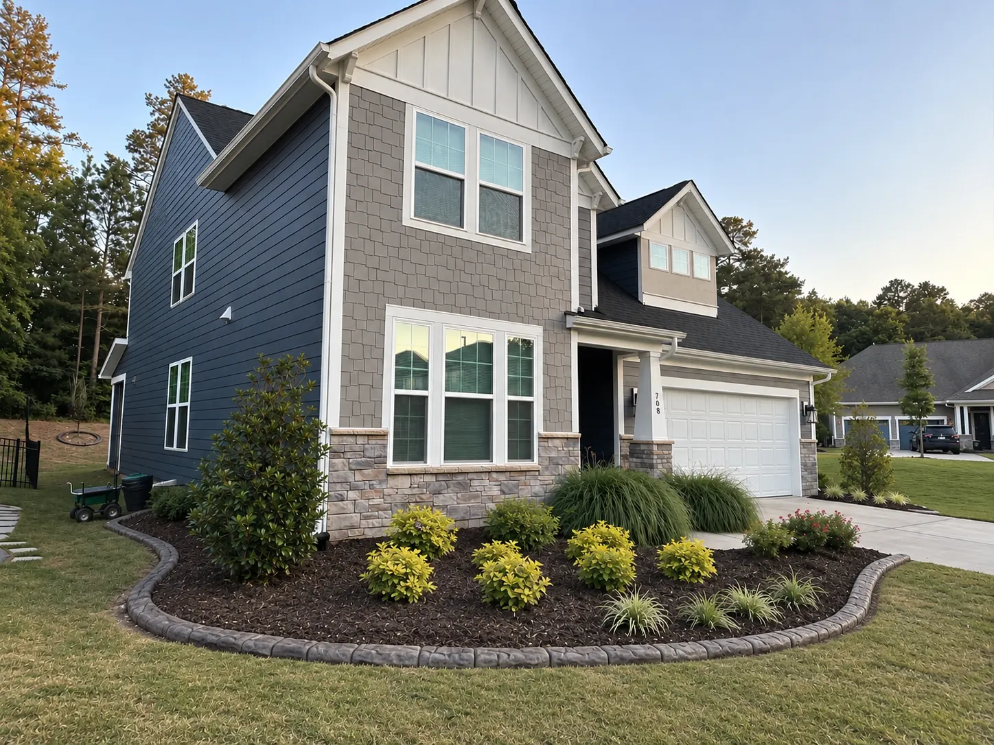 Two-story navy house at dusk with a kidney-shaped mulched bed and a poured curb