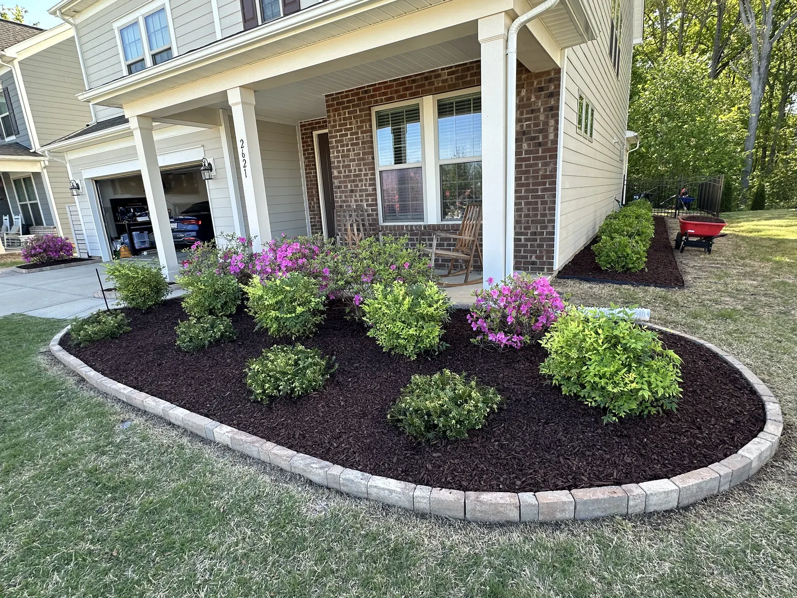 An oval mulched bed with azaleas and a light poured curb in front of a porch