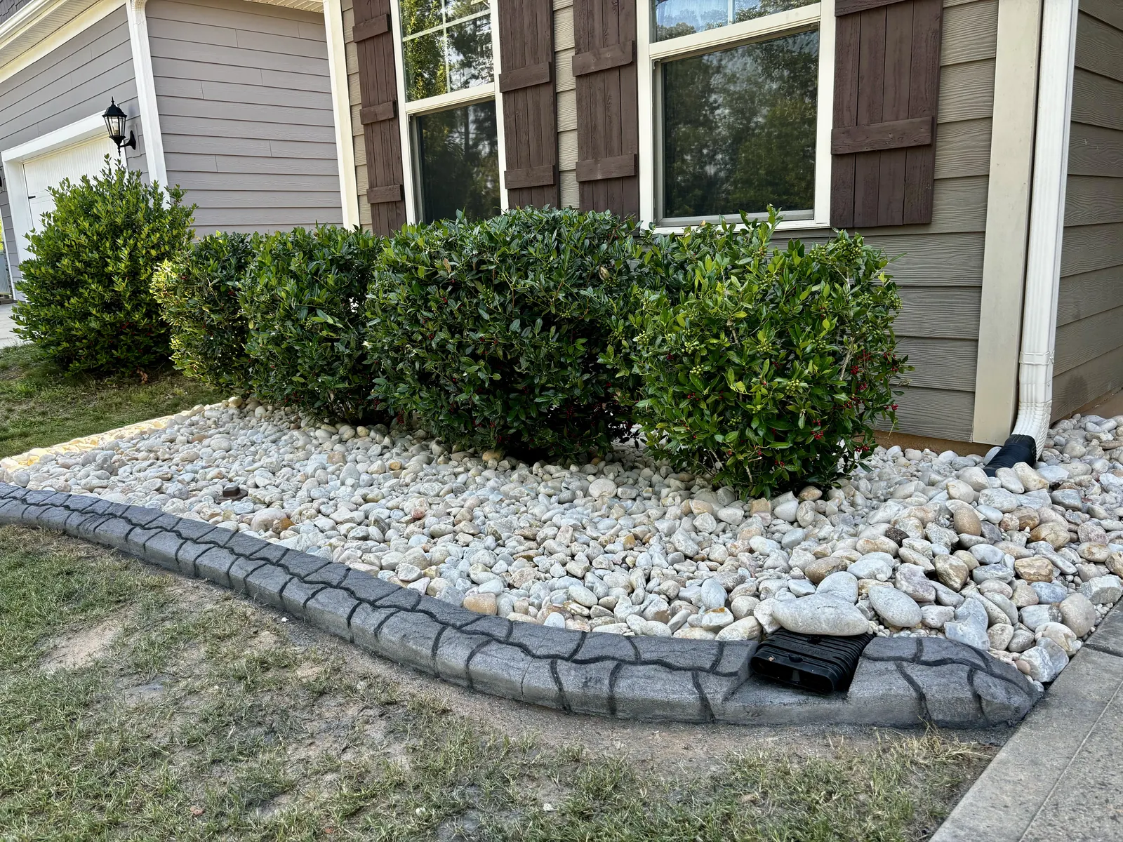 Stamped concrete curb with river rock, shrubs and a built-in rain drain